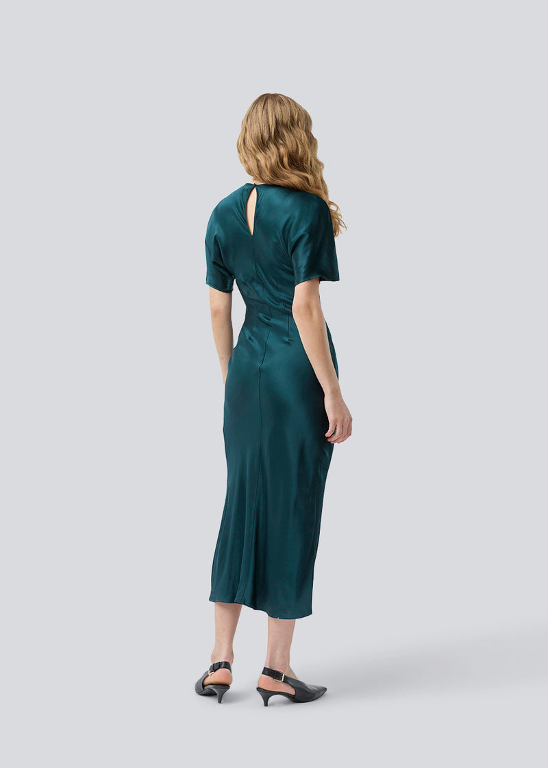 Grøn lang kjole i satin med draperingsdetalje. Parveenmd dress har korte ærmer og en usynlig lynlås i ryggen. Modellen er 175 cm og har en str. s/36 på.