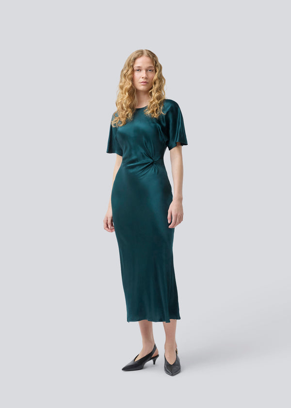 Grøn lang kjole i satin med draperingsdetalje. Parveenmd dress har korte ærmer og en usynlig lynlås i ryggen. Modellen er 175 cm og har en str. s/36 på.