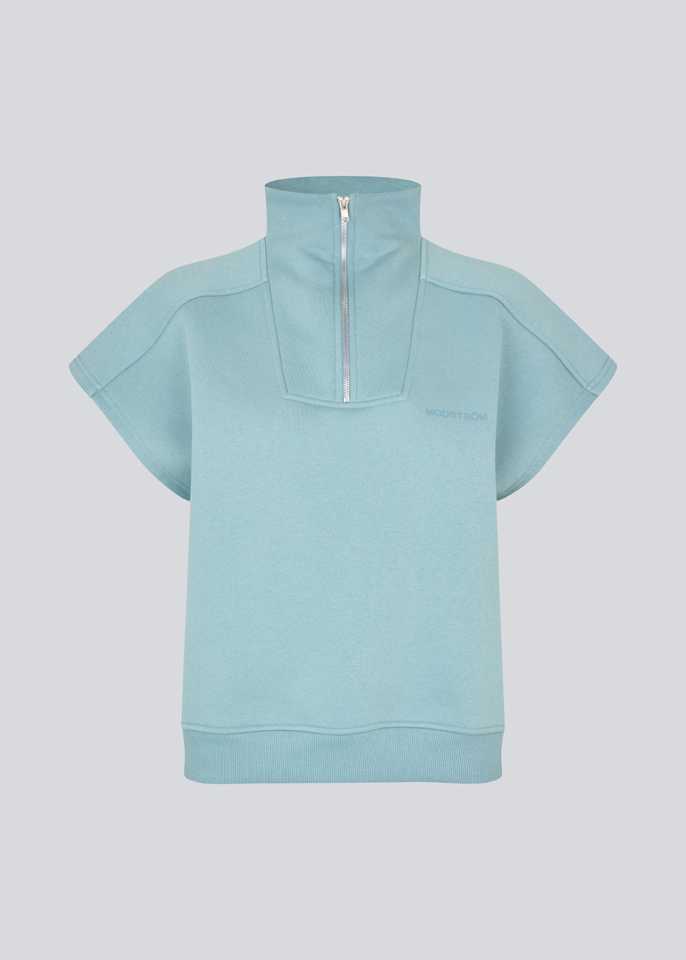 Kortærmet sweatshirt i lyseblå med et sporty twist. PaulaMD SS T-neck har høj hals med lynlås, så du kan vælge mellem et cool højt look eller en mere åben og afslappet stil. Detaljer som brystlogo og ribkant i bunden giver et rent og moderne udtryk.