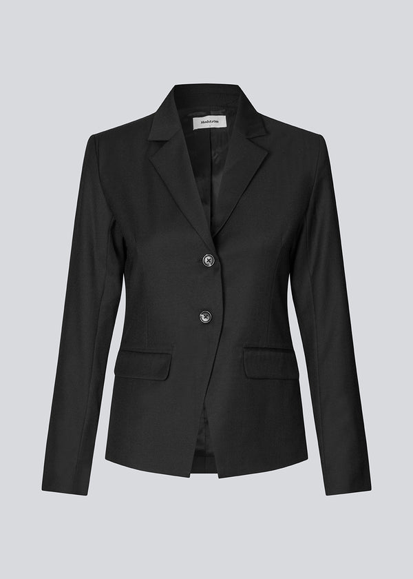 Let figursyet blazer i sort med v-udskæring og knappelukning fortil. Piloumd blazer har to lommer fortil og en slids ved ærmet med knappelukning.&nbsp;