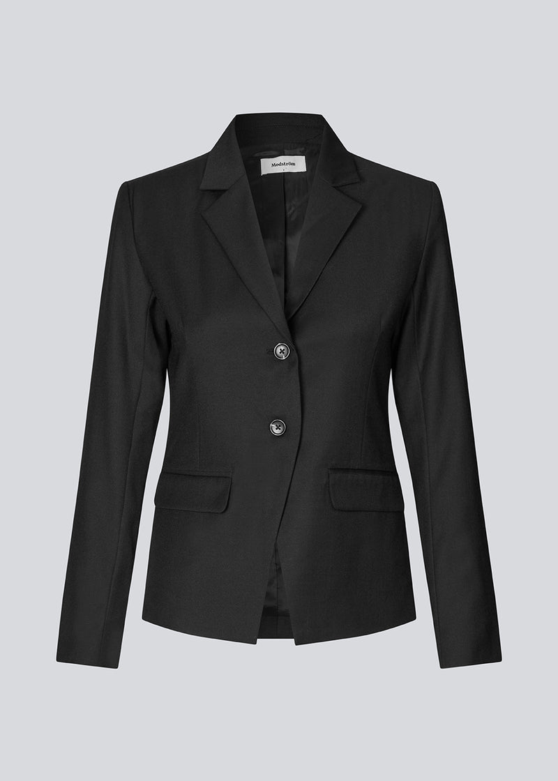 Let figursyet blazer i sort med v-udskæring og knappelukning fortil. Piloumd blazer har to lommer fortil og en slids ved ærmet med knappelukning.&nbsp;