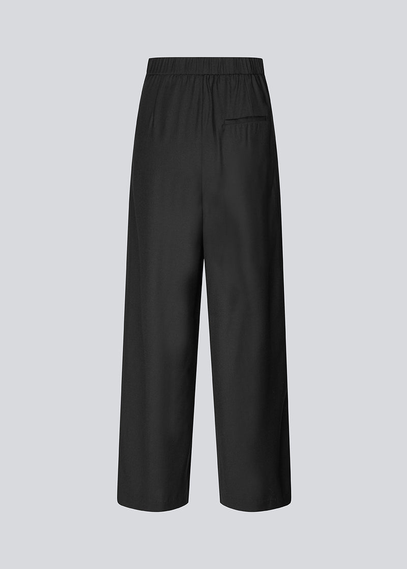 Sorte bukser med brede ben, læg og elastisk talje. Piloumd pants har sidelommer og en lynlås med knappelukning i siden. Modellen er 175 cm og har en str S/36 &nbsp;på.
