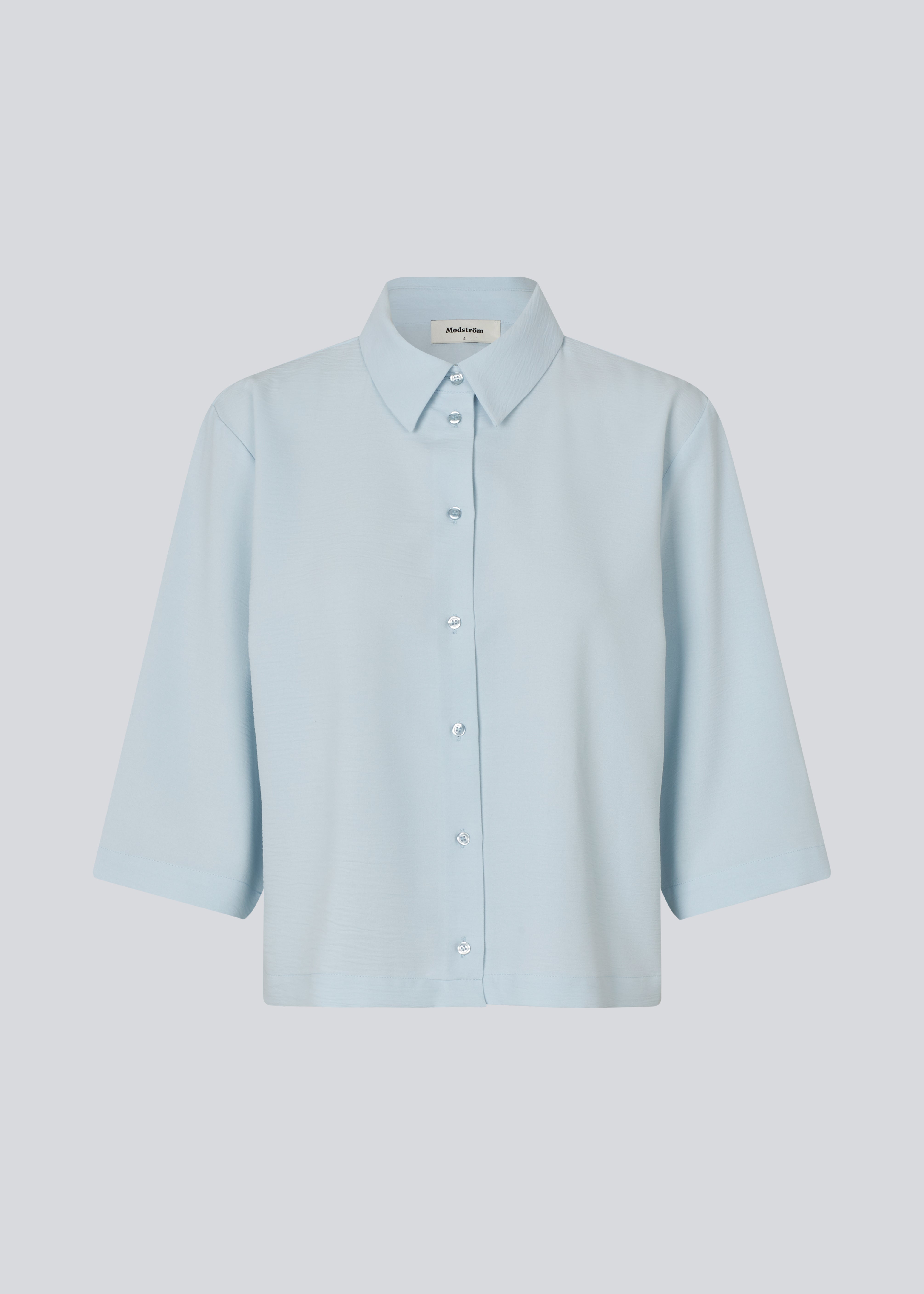 Skjorte med 3/4 ærmer i 100% genanvendt polyester i lyseblå. Popelmd shirt har en løspasform med knappelukning og skjortekrave.&nbsp;