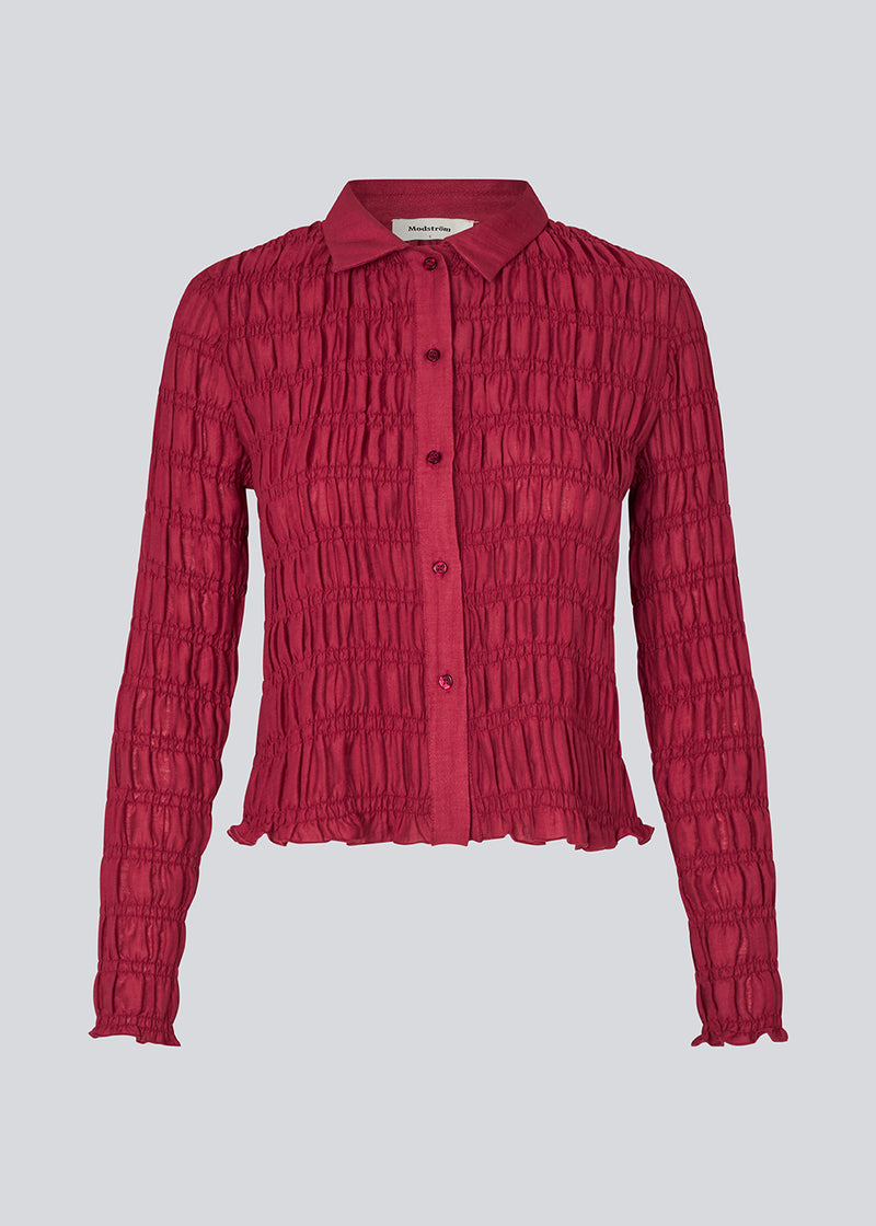 Langærmet tætsiddende top i mørkerød med smock. Posiemd shirt har en knappelukning fortil og skjorte krave. Modellen er 175 cm og har en str S/36 på.