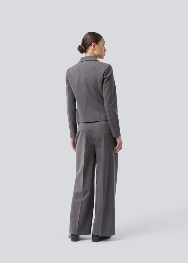 Grå kort figursyet blazer. Primrosemd blazer har knappelukning og to lommer fortil. Modellen er 175 cm og har en str. s/36 på.
