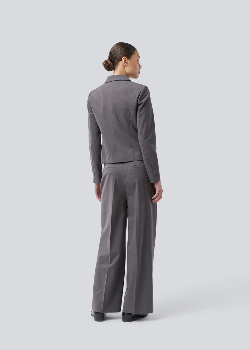 Grå kort figursyet blazer. Primrosemd blazer har knappelukning og to lommer fortil. Modellen er 175 cm og har en str. s/36 på.