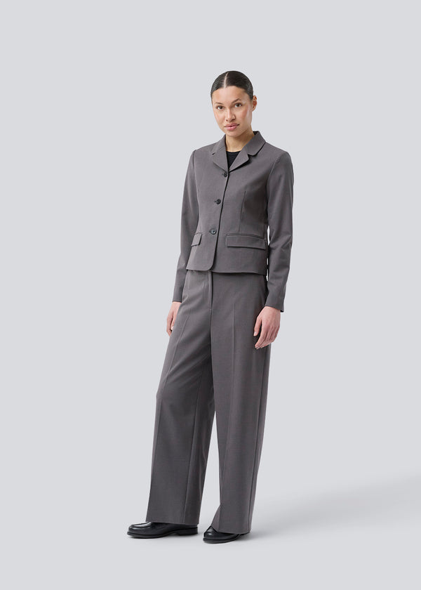 Grå kort figursyet blazer. Primrosemd blazer har knappelukning og to lommer fortil. Modellen er 175 cm og har en str. s/36 på.