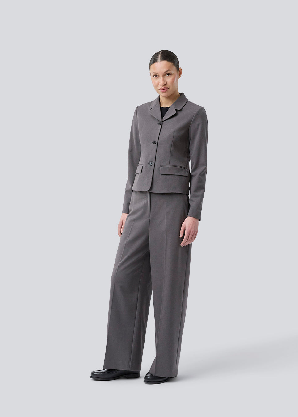 Grå kort figursyet blazer. Primrosemd blazer har knappelukning og to lommer fortil. Modellen er 175 cm og har en str. s/36 på.