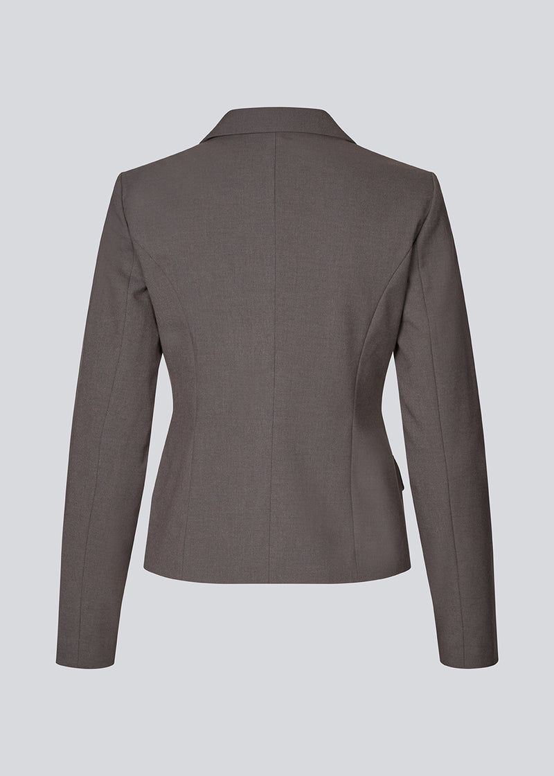 Grå kort figursyet blazer. Primrosemd blazer har knappelukning og to lommer fortil. Modellen er 175 cm og har en str. s/36 på.