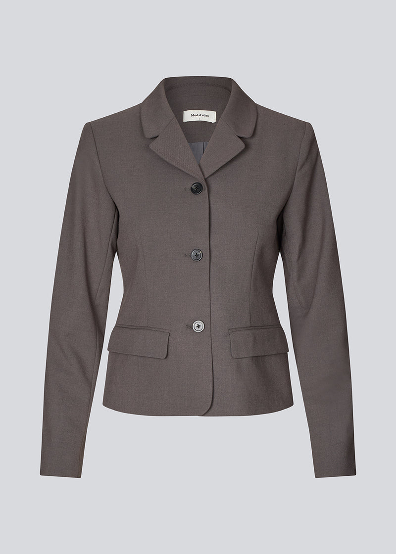 Grå kort figursyet blazer. Primrosemd blazer har knappelukning og to lommer fortil. Modellen er 175 cm og har en str. s/36 på.