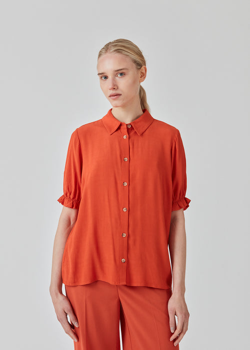 Rød skjorte med korte, puffede ærmer med elastisk kant. RavenMD print shirt har normal krave og knapper foran. Pasformen er afslappet. Modellen er 173 cm og har en størrelse S/36 på
