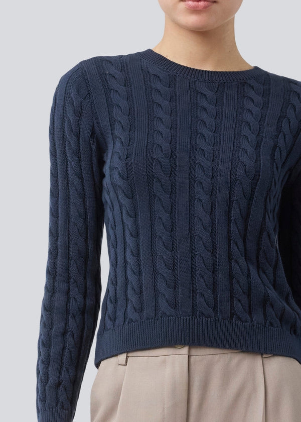 Tætsiddende strik med rund hals i 100% økologisk bomuld. Sabremd o-neck er lavet i kabelstrik og har et broderet brystlogo. Modellen er 175 cm og har en str s/36 på.
