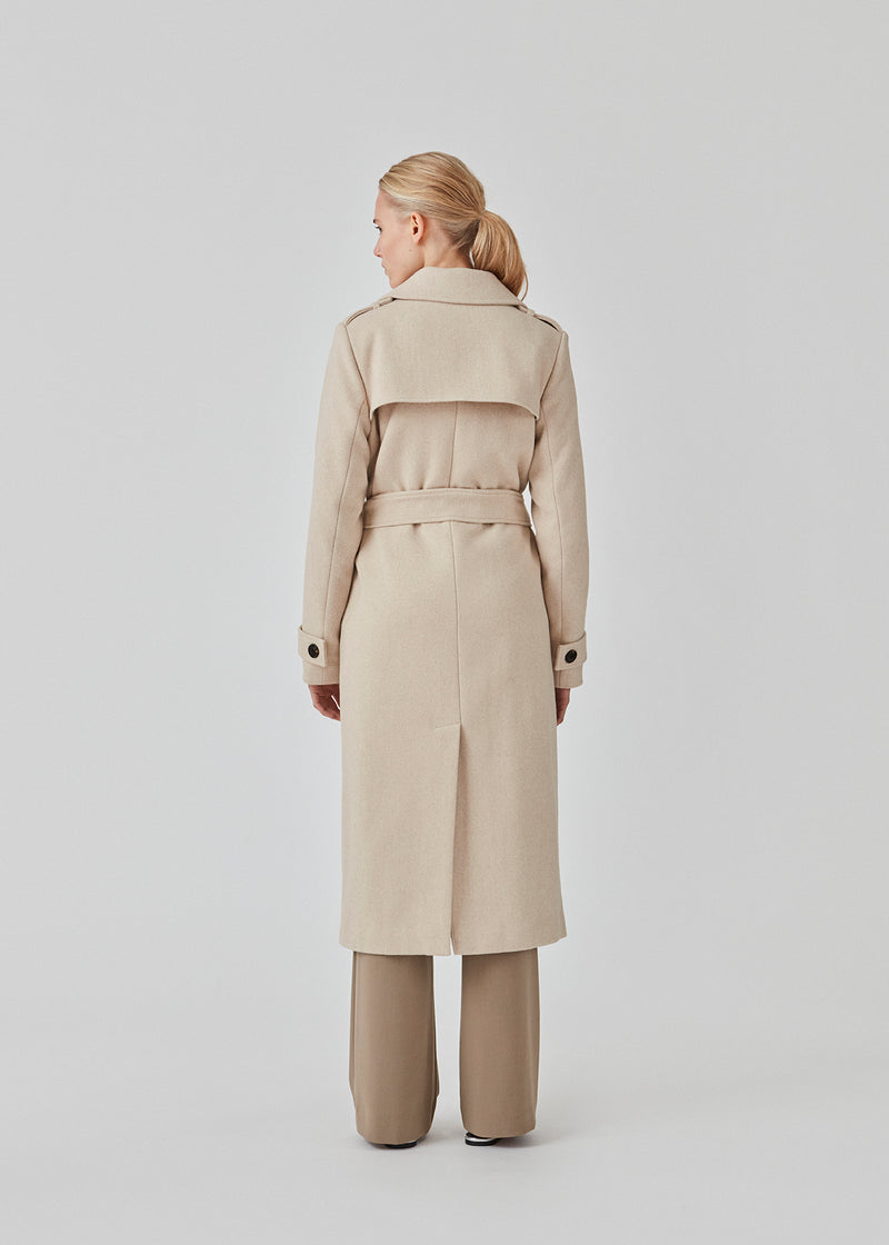 Klassisk, dobbeltradet uldfrakke i beige med krave og revers. ShayMD coat har bredt taljebælte, skulderstropper, brede manchetter og stormflap. Med for og slids bagpå.
