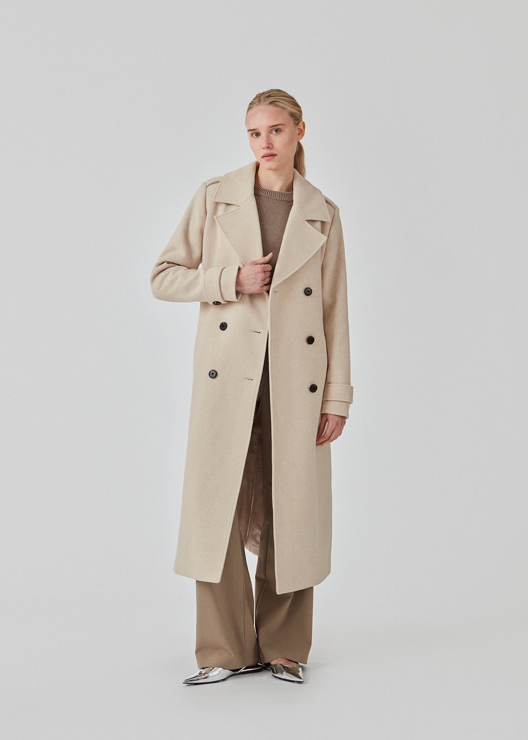 Klassisk, dobbeltradet uldfrakke i beige med krave og revers. ShayMD coat har bredt taljebælte, skulderstropper, brede manchetter og stormflap. Med for og slids bagpå.