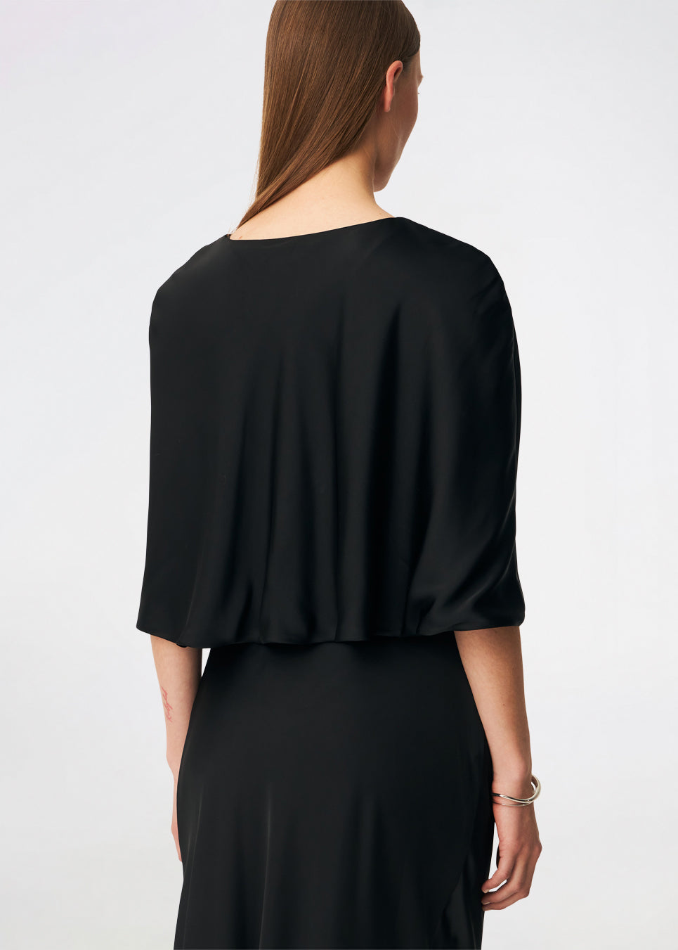 Tailormd Cape er en elegant satin-cape, der tilfører et raffineret og dramatisk udtryk til ethvert outfit. Designet falder let over skuldrene og lukkes foran med en dekorativ knudedetalje, som skaber et blødt, flydende fald. Brug den over en kjole til særlige anledninger eller som et eksklusivt lag over en enkel top for et sofistikeret look.&nbsp;