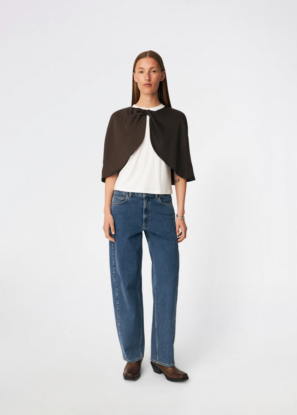Tailormd Cape er en elegant satin-cape, der tilfører et raffineret og dramatisk udtryk til ethvert outfit. Designet falder let over skuldrene og lukkes foran med en dekorativ knudedetalje, som skaber et blødt, flydende fald. Brug den over en kjole til særlige anledninger eller som et eksklusivt lag over en enkel top for et sofistikeret look. Modellen er 175 cm høj og bruger størrelse S/36.