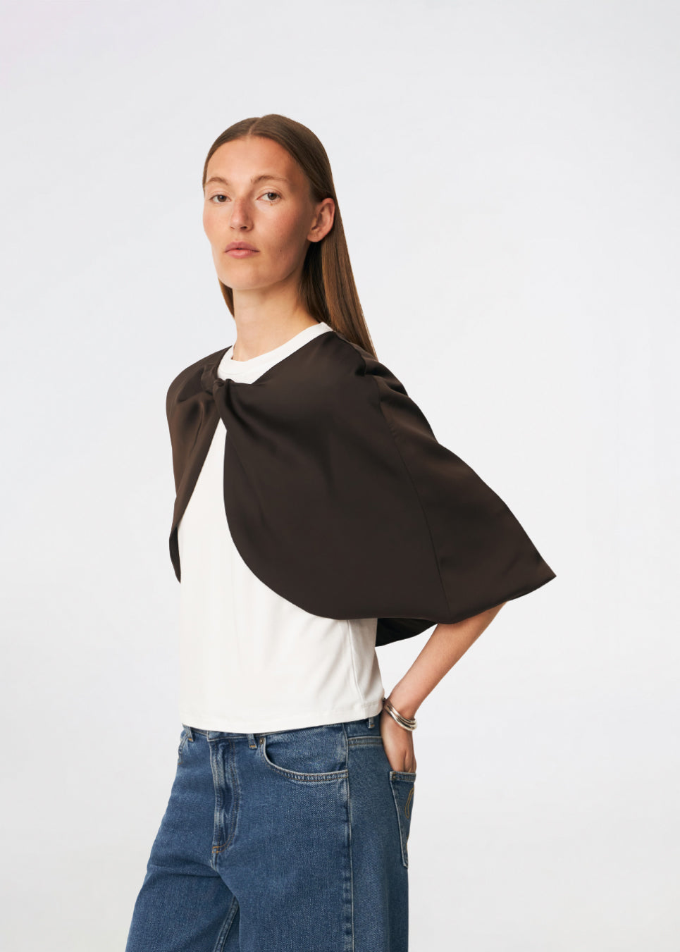 Tailormd Cape er en elegant satin-cape, der tilfører et raffineret og dramatisk udtryk til ethvert outfit. Designet falder let over skuldrene og lukkes foran med en dekorativ knudedetalje, som skaber et blødt, flydende fald. Brug den over en kjole til særlige anledninger eller som et eksklusivt lag over en enkel top for et sofistikeret look. Modellen er 175 cm høj og bruger størrelse S/36.