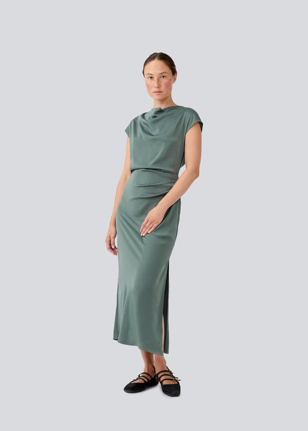 Lang ærmeløs kjole i smuk grøn med rynkedetalje i satin. TailorMD dress har en høj hals, usynlig lynlås i ryggen og en slids i siden. Modellen er 177 cm og har en str S/36 på.