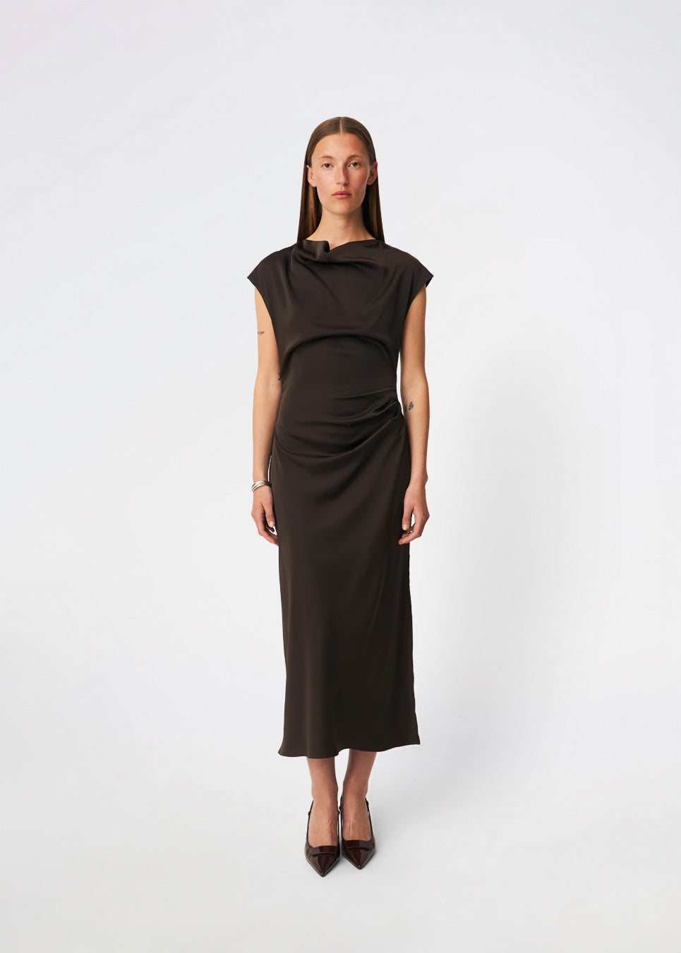 Elegant satinmaxikjole med et sofistikeret udtryk. Tailormd dress er designet i en figursyet silhuet med en blød draperet halsudskæring, korte cap-ærmer og diskrete rynkedetaljer i taljen, der fremhæver den flatterende pasform. Den glatte satinfinish og den lange, flydende silhuet gør kjolen til et elegant valg til både festlige anledninger og særlige begivenheder. Modellen er 175 cm og har en str S/36 på.