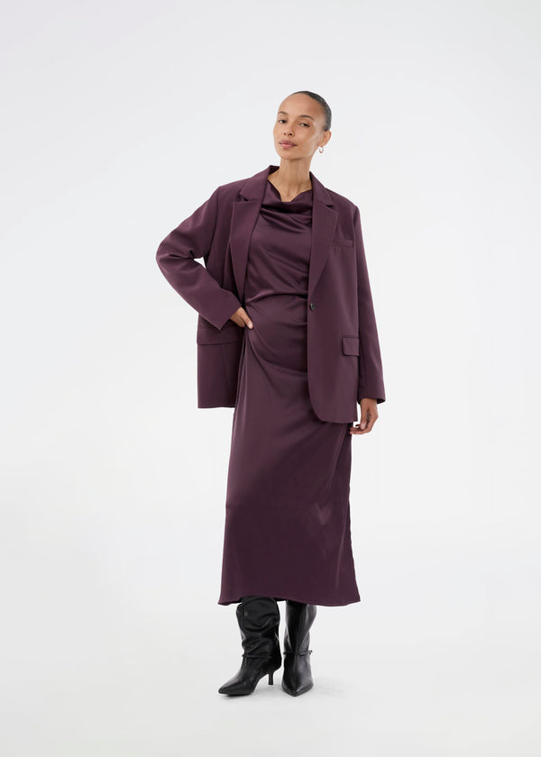 Mørklilla lang ærmeløs kjole med rynkedetalje i satin. TailorMD dress har en høj hals, usynlig lynlås i ryggen og en slids i siden. Modellen er 175 cm og har en str S/36 på.
