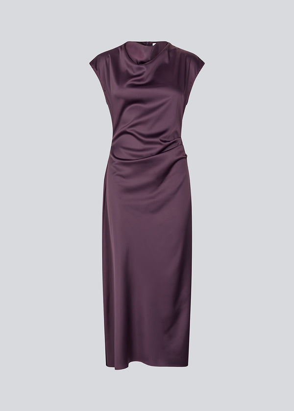 Mørklilla lang ærmeløs kjole med rynkedetalje i satin. TailorMD dress har en høj hals, usynlig lynlås i ryggen og en slids i siden. Modellen er 175 cm og har en str S/36 på.
