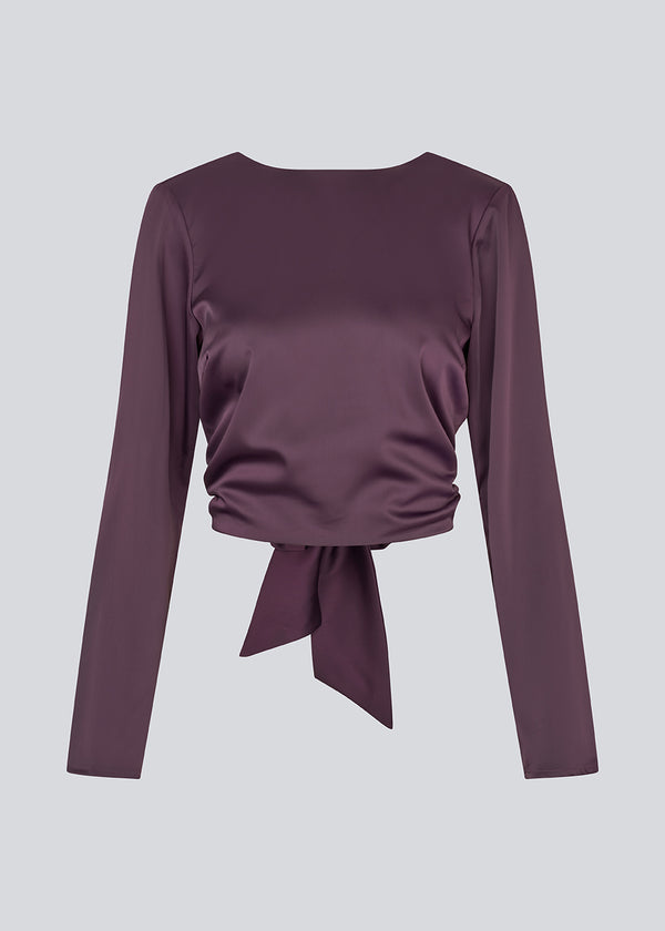 Langærmet top i satin. TailotMD top &nbsp;har en flatterende åben ryg og bindebånd, der giver den et elegant og feminint udtryk. Modellen er 177 cm og har en str S/36 på.