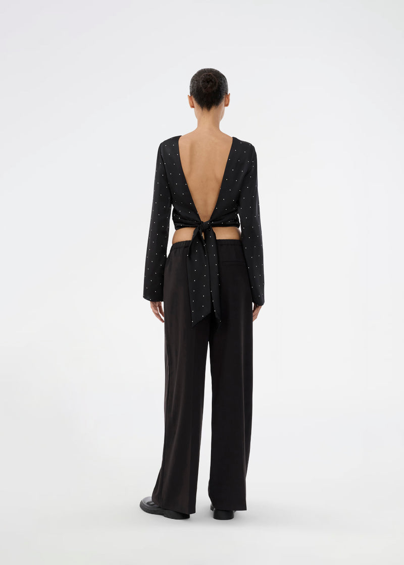 Langærmet top i satin i sort med hvide små prikker. Tailormd print LS top har en flatterende åben ryg og bindebånd, der giver den et elegant og feminint udtryk. Modellen er 177 cm og har en str S/36 på.