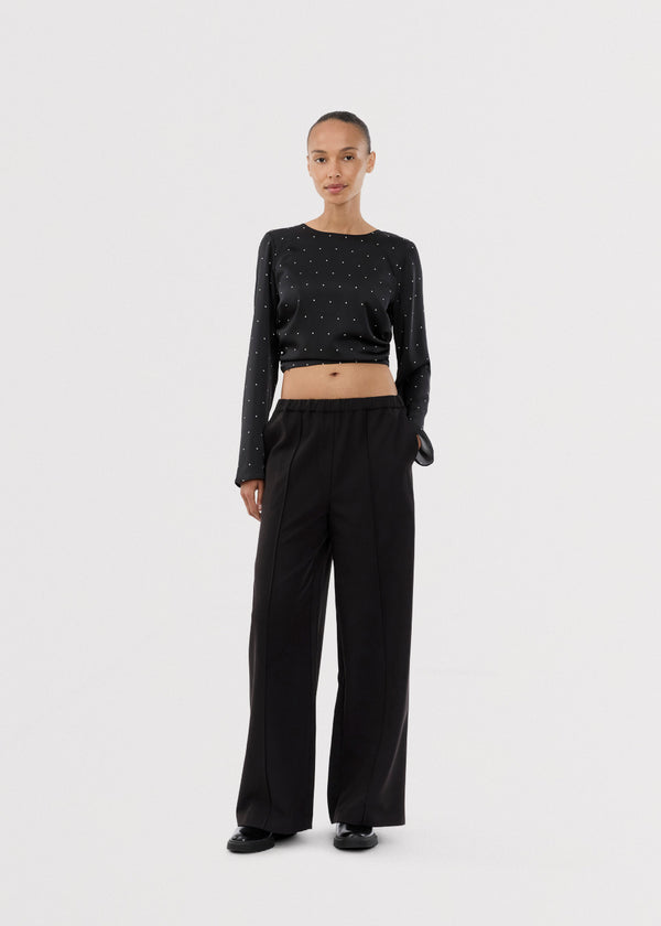 Langærmet top i satin i sort med hvide små prikker. Tailormd print LS top har en flatterende åben ryg og bindebånd, der giver den et elegant og feminint udtryk. Modellen er 177 cm og har en str S/36 på.