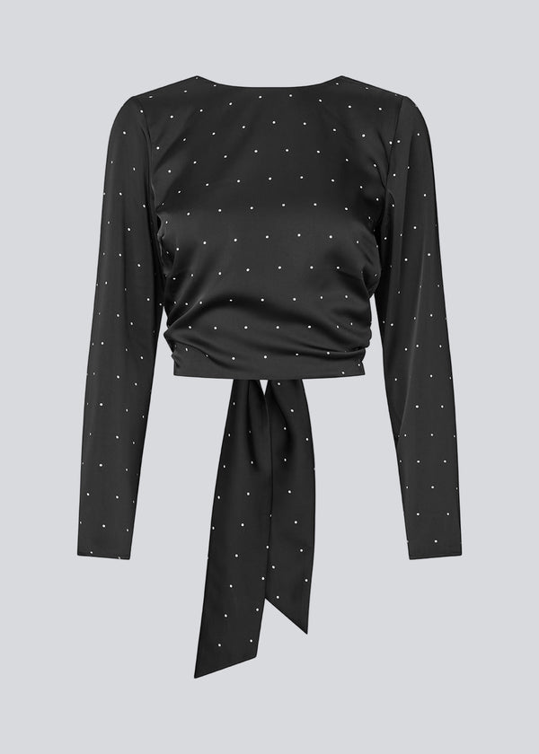 Langærmet top i satin i sort med hvide små prikker. Tailormd print LS top har en flatterende åben ryg og bindebånd, der giver den et elegant og feminint udtryk. Modellen er 177 cm og har en str S/36 på.