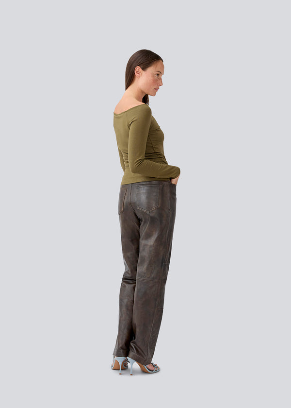 Tansy LS top i mørkegrøn har et enkelt udtryk med en bred halsudskæring og lange, smalle ærmer. Toppen har en tætsiddende pasform. Modellen er 173 cm og har en størrelse S/36 på.