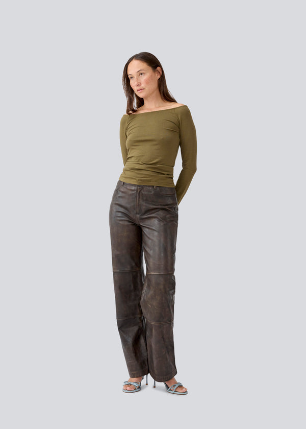 Tansy LS top i mørkegrøn har et enkelt udtryk med en bred halsudskæring og lange, smalle ærmer. Toppen har en tætsiddende pasform. Modellen er 173 cm og har en størrelse S/36 på.