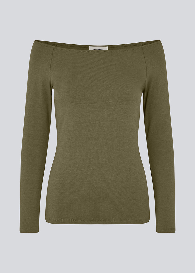 Tansy LS top i mørkegrøn har et enkelt udtryk med en bred halsudskæring og lange, smalle ærmer. Toppen har en tætsiddende pasform. Modellen er 173 cm og har en størrelse S/36 på.