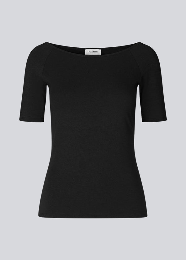 Tansy top i farven sort har et enkelt udtryk med en bred udskæring både for og bag og har smalle ærmer. Toppen er en smal model, der sidder tæt uden at være stram.