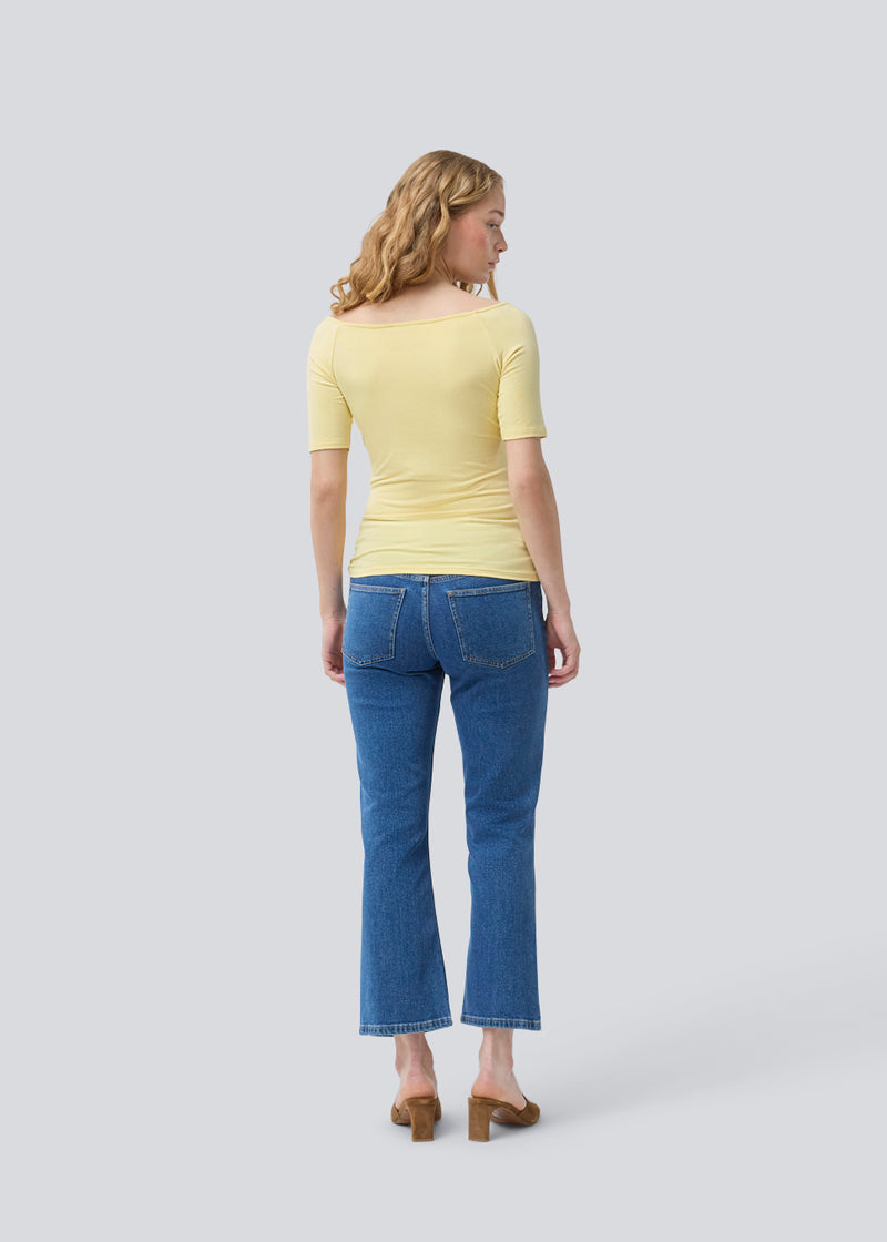 Tansy top i gul har et enkelt udtryk med en bred udskæring både for og bag og har smalle ærmer. Toppen er en smal model, der sidder tæt uden at være stram. Modellen er 175 cm og har en størrelse S/36 på
