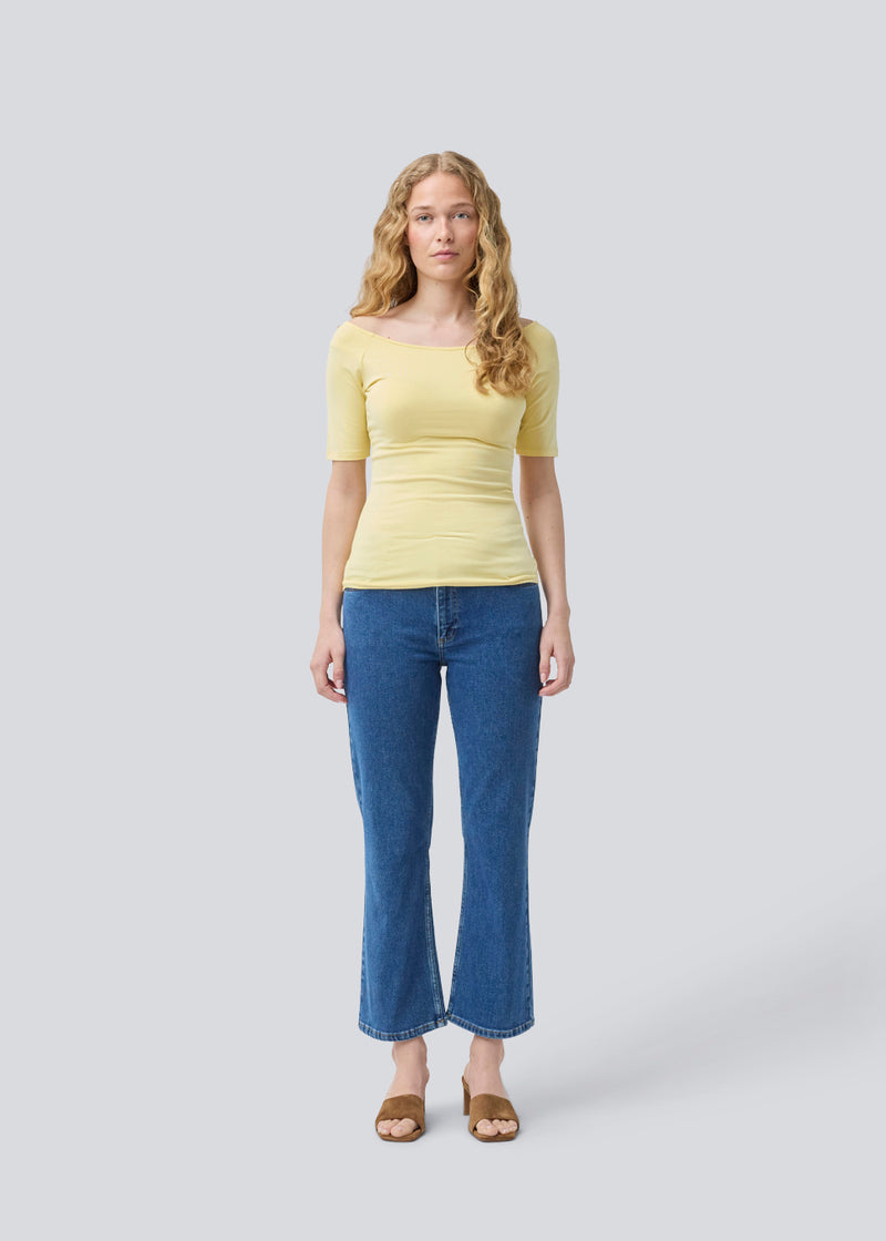 Tansy top i gul har et enkelt udtryk med en bred udskæring både for og bag og har smalle ærmer. Toppen er en smal model, der sidder tæt uden at være stram. Modellen er 175 cm og har en størrelse S/36 på
