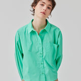 Skjorte i farven Calm Jade i økologisk bomuldspoplin med cropped længde. TapirMD cropped shirt har krave og knapper foran, samt brystlomme. Lav skuldersøm og lange ærmer med manchet og knap. Broderet logo foran. Modellen er 177 cm og har en størrelse S/36 på.