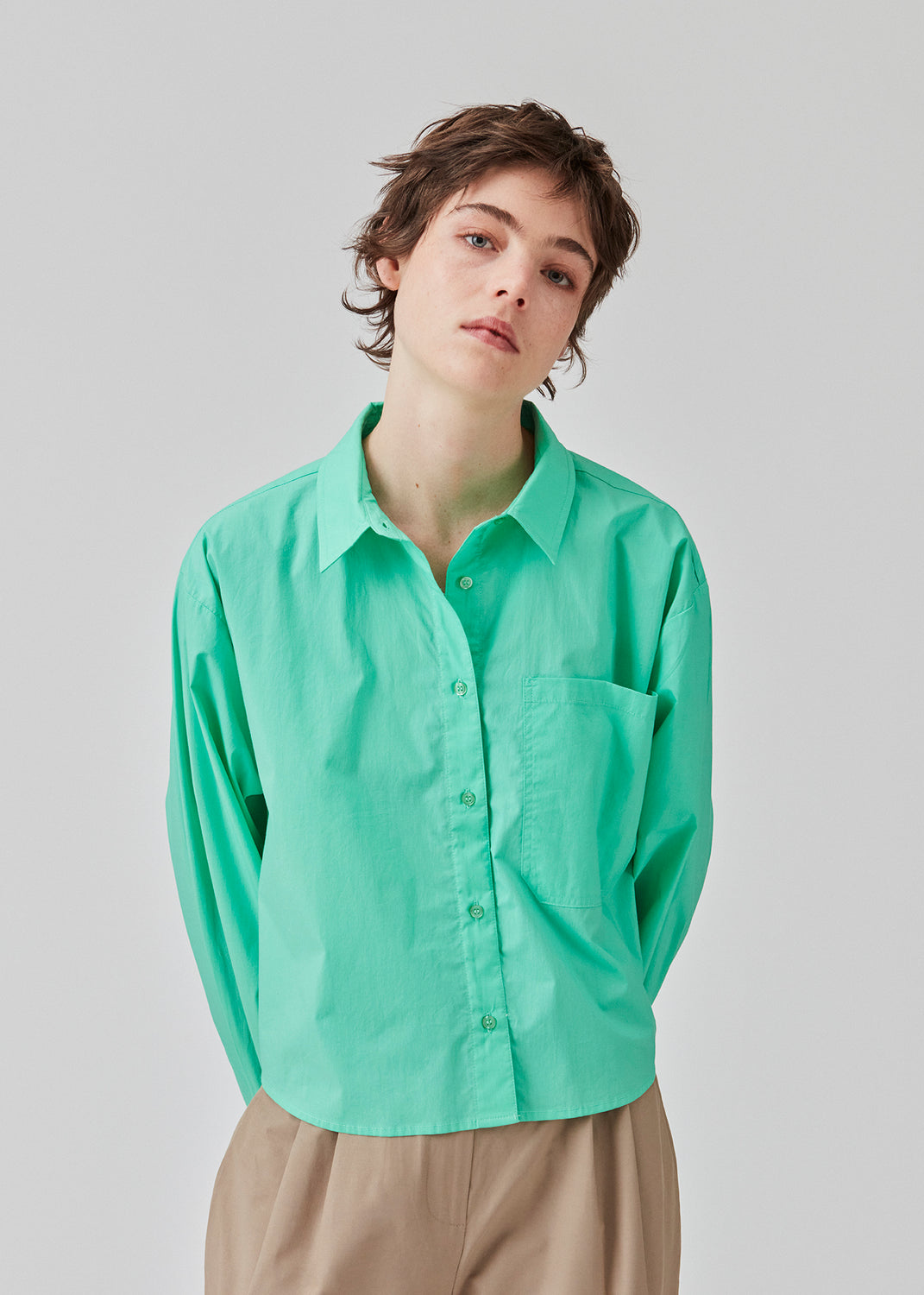 Skjorte i farven Calm Jade i økologisk bomuldspoplin med cropped længde. TapirMD cropped shirt har krave og knapper foran, samt brystlomme. Lav skuldersøm og lange ærmer med manchet og knap. Broderet logo foran. Modellen er 177 cm og har en størrelse S/36 på.