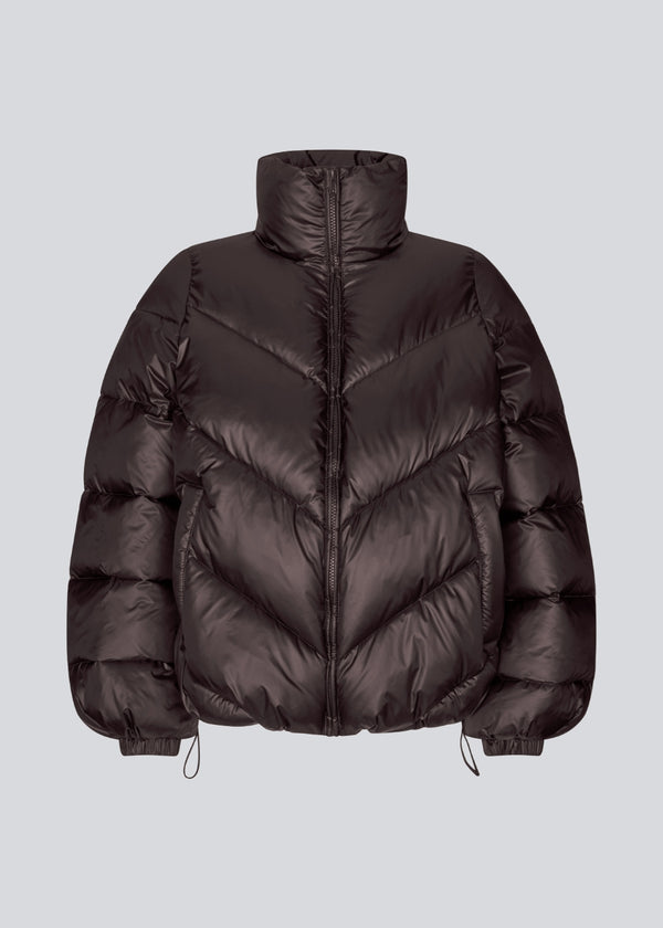 Brun dunjakke med høj hals i 100% genanvendt polyester.&nbsp; Tetrismd jacket har en lynlåslukning og en justerbar elastik i ærmet. Modellen er 175 cm og har en str. s/36 på.