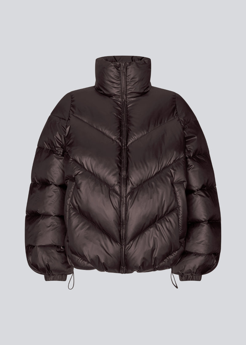 Brun dunjakke med høj hals i 100% genanvendt polyester.&nbsp; Tetrismd jacket har en lynlåslukning og en justerbar elastik i ærmet. Modellen er 175 cm og har en str. s/36 på.