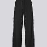 Loose black trousers with wide legs and a relaxed fit. Featuring an elastic waistband with drawstring for a comfortable, adjustable waist. White side stripes add a sporty and modern touch to the otherwise classic design. Perfect for casual everyday wear or more elevated styling – easy to pair with everything from t-shirts to dressy tops.