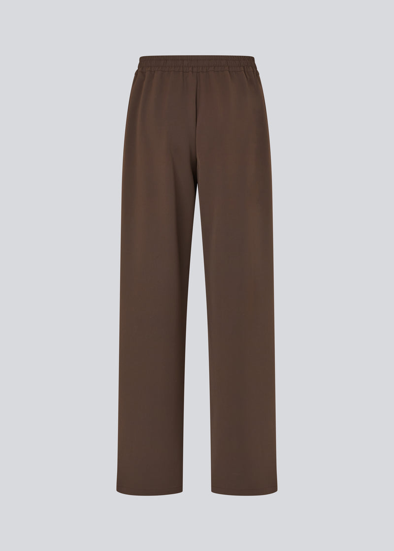 Løse brune bukser med bred benvidde og afslappet pasform. Bukserne har elastisk linning med snøre, der sikrer en behagelig og justerbar talje. Langs siderne løber hvide striber, som tilføjer et sporty og moderne twist til det ellers klassiske design. Perfekte til både afslappet hverdagsbrug og mere stilfulde outfits – nemme at style med alt fra t-shirts til skjorter.
