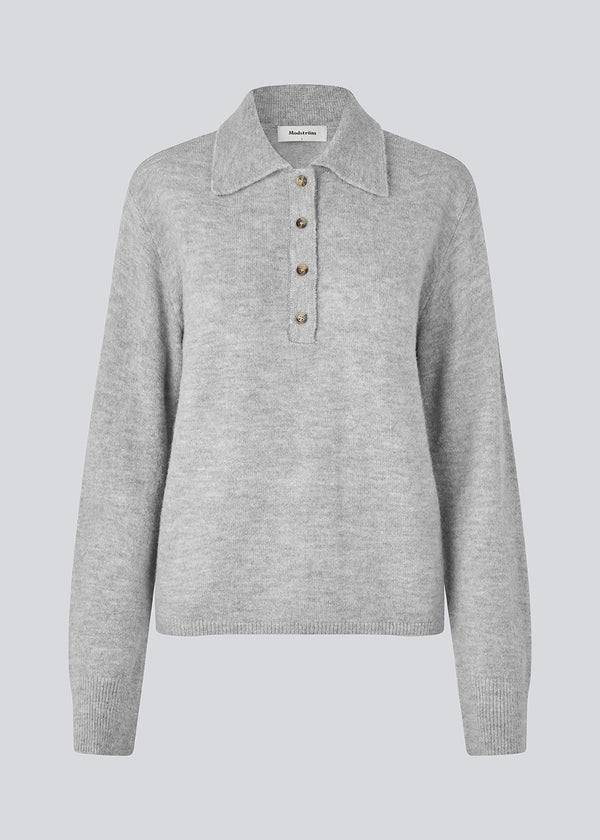 Strikket polo i grå med lange brede ærmer. Treemd polo har en stolpelukning og 4 knapper. Modellen er 175 cm og har en str. S/36 på.