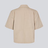 Kortærmet beige blazer med enkeltradet lukning. TuesdayMD SS Blazer har en krydsende knaplukning, krave, sidelommer og en falsk brystlomme – et moderne twist på en tidløs klassiker. Kan bæres lukket som en elegant top eller åben over en let bluse for et mere afslappet udtryk.&nbsp;
