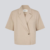 Kortærmet beige blazer med enkeltradet lukning. TuesdayMD SS Blazer har en krydsende knaplukning, krave, sidelommer og en falsk brystlomme – et moderne twist på en tidløs klassiker. Kan bæres lukket som en elegant top eller åben over en let bluse for et mere afslappet udtryk.&nbsp;