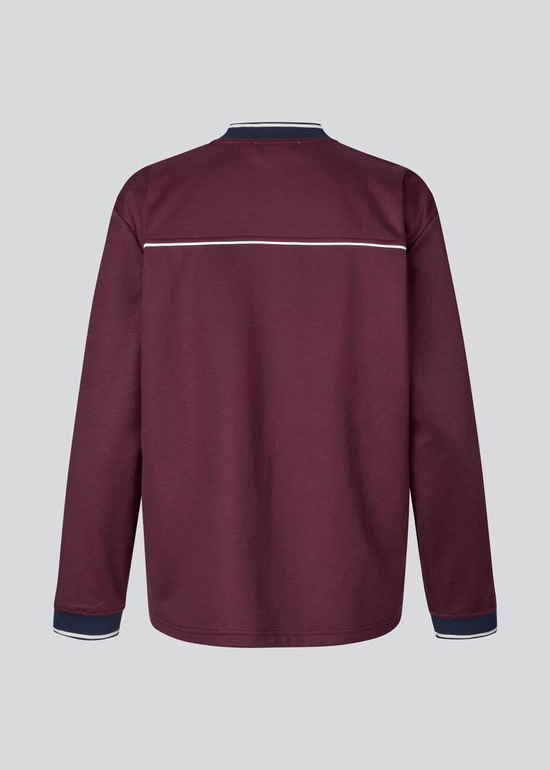 Mørkerød tracksuit trøje i 100% genanvendt polyester. Utopiamd LS t-shirt har lange ærmer, v-hals med kontrastdetaljer samt logo foran.