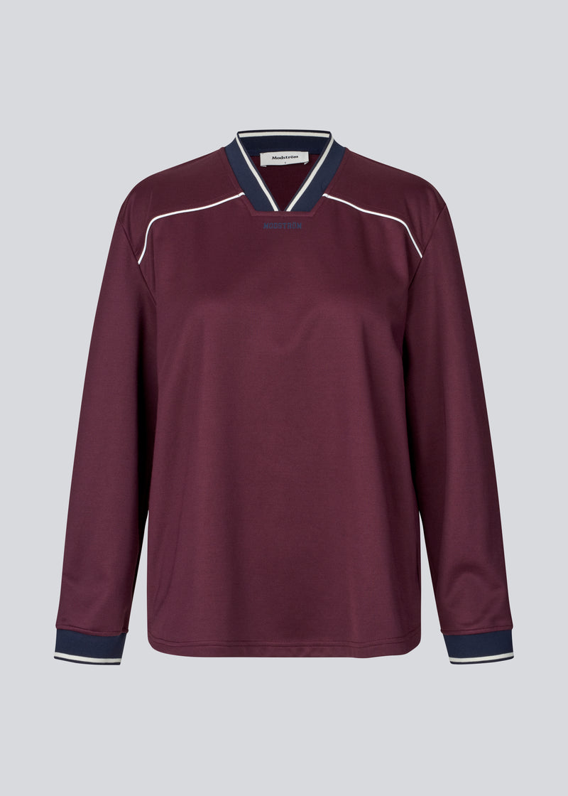 Mørkerød tracksuit trøje i 100% genanvendt polyester. Utopiamd LS t-shirt har lange ærmer, v-hals med kontrastdetaljer samt logo foran.