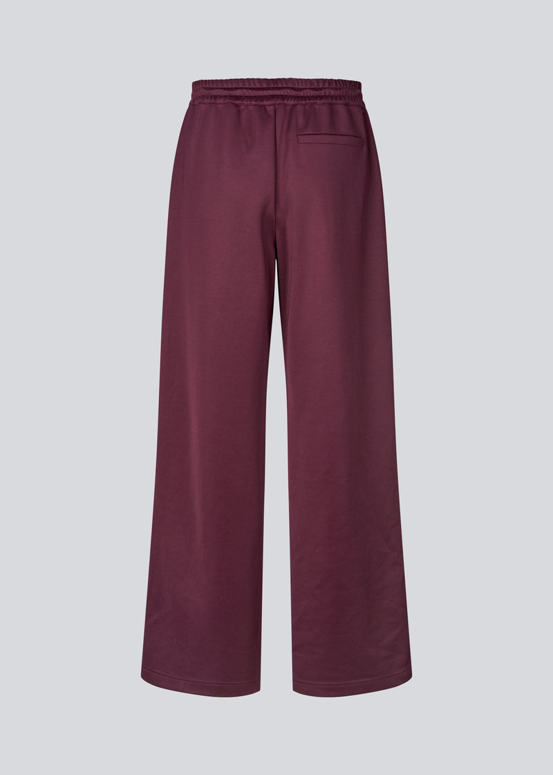 Mørkerøde tracksuit pants med brede ben i 100% genanvendt polyester. Utopiamd pants har sidelommer, elastik i talje med snørre og logo.