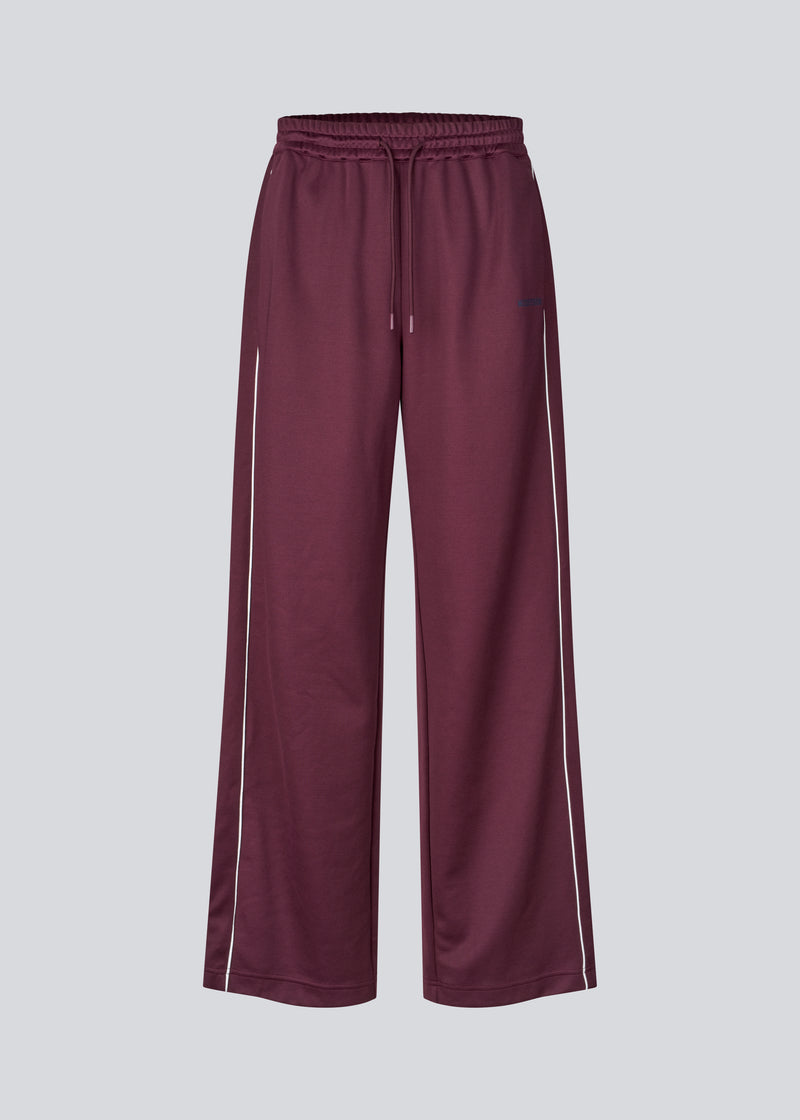 Mørkerøde tracksuit pants med brede ben i 100% genanvendt polyester. Utopiamd pants har sidelommer, elastik i talje med snørre og logo.