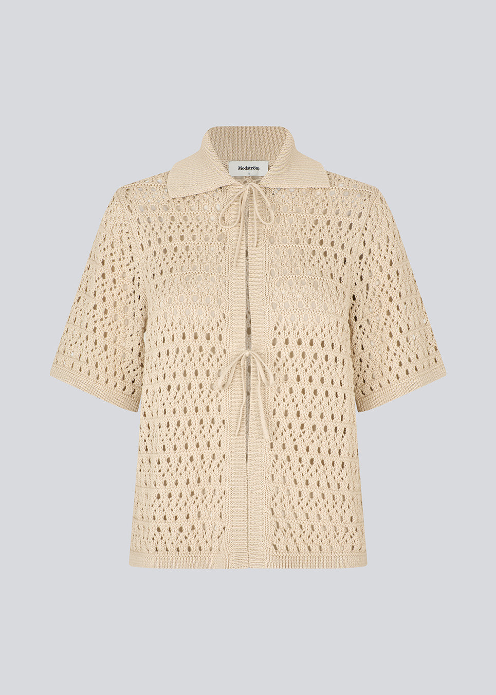 Elegant og let cardigan i et smukt strikket hulmønster. VesterMD cardigan har korte ærmer, krave og justerbar snørelukning foran, der giver et feminint og afslappet udtryk. Fremstillet i 100% økologisk bomuld for en blød og åndbar komfort.