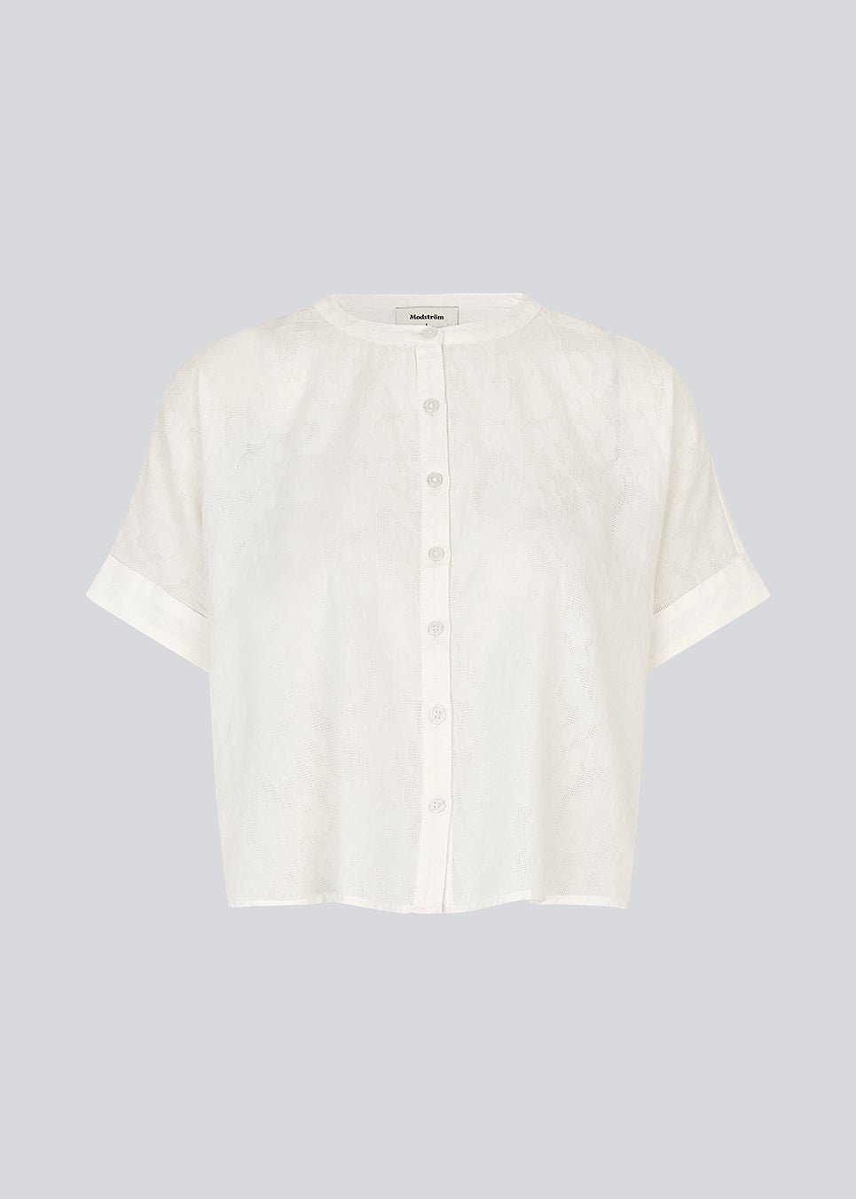 Kortærmet skjorte-bluse i hvid med ensfarvet print. VilleminMD shirt har knappelukning, rund halsudskæring og opsmøg på ærmerne, og længden går til buksekanten. Et tidløst og elegant valg, der nemt kan styles både til hverdag og aften.